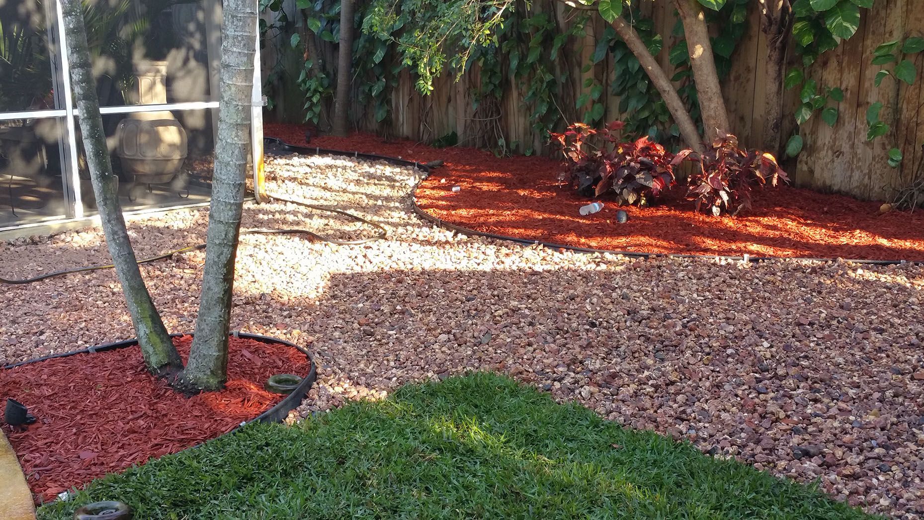 A backyard with a fence , trees , and red mulch.