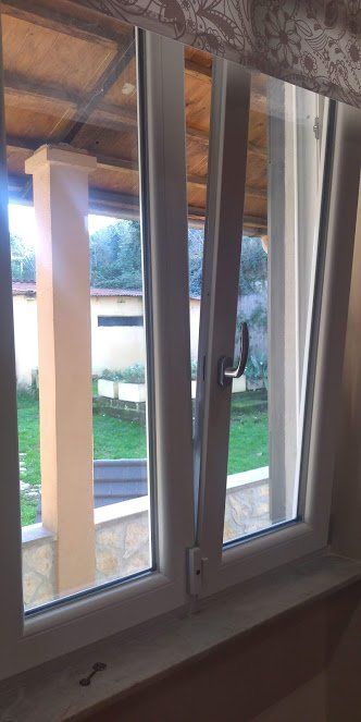 Apri la finestra bianca, rivelando l'erba verde e il pilastro beige all'esterno.