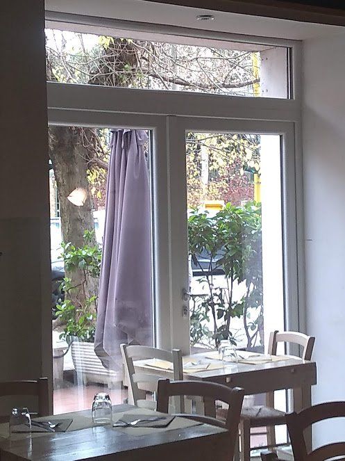 Interno del ristorante con vista sugli alberi esterni attraverso una finestra a doppia porta; tenda, tavoli e sedie viola.