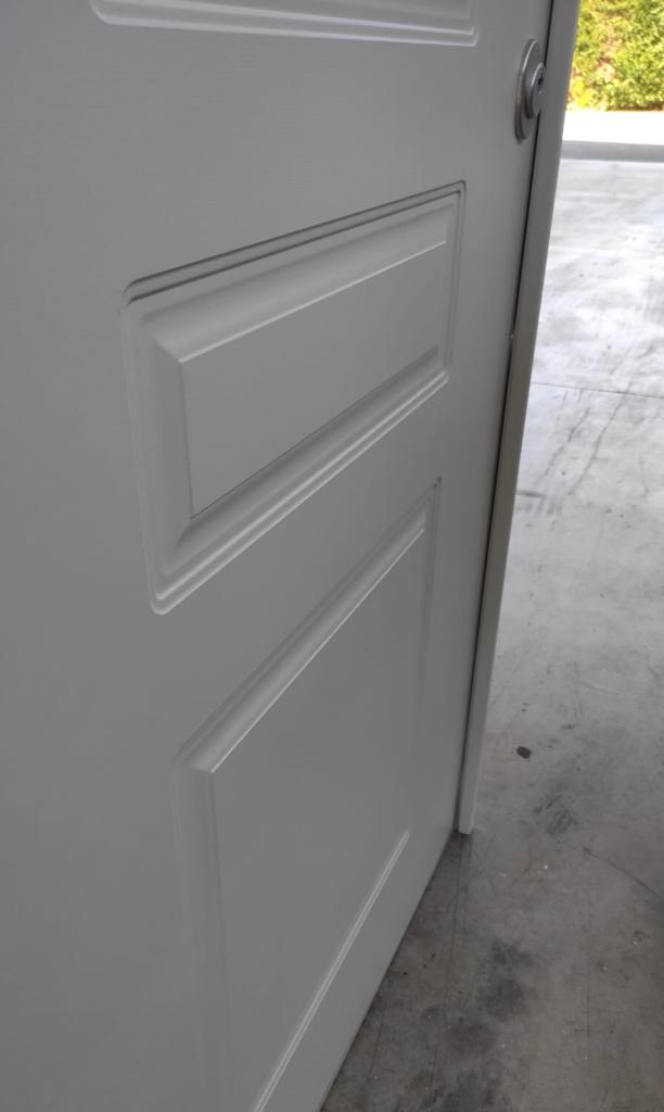 Porta bianca con due pannelli rettangolari, leggermente socchiusi, appoggiati a un pavimento di cemento.