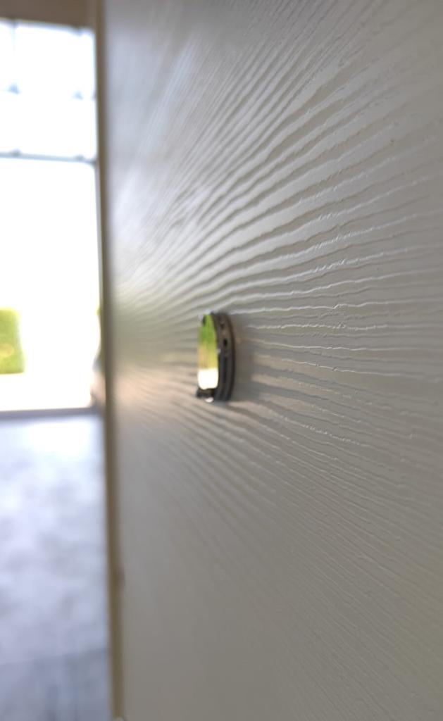 Primo piano di una parete bianca testurizzata con un piccolo oggetto scuro e circolare che sporge verso l'esterno.