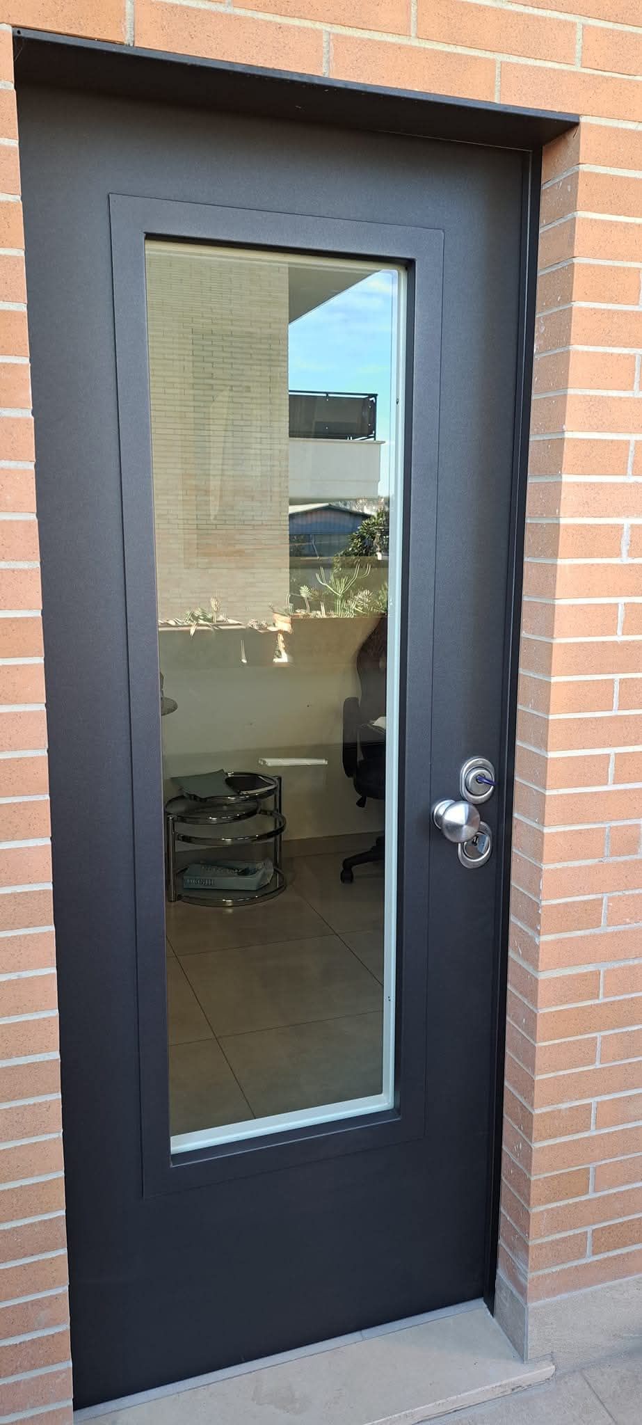 Porta nera con pannello di vetro incastonato in un muro di mattoni.