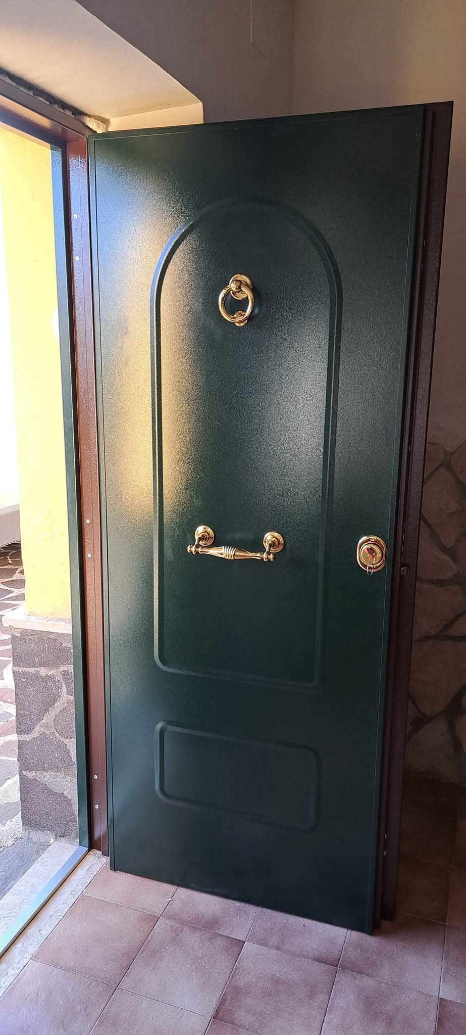 Porta d'ingresso verde con ferramenta dorata socchiusa, nell'ingresso in pietra.