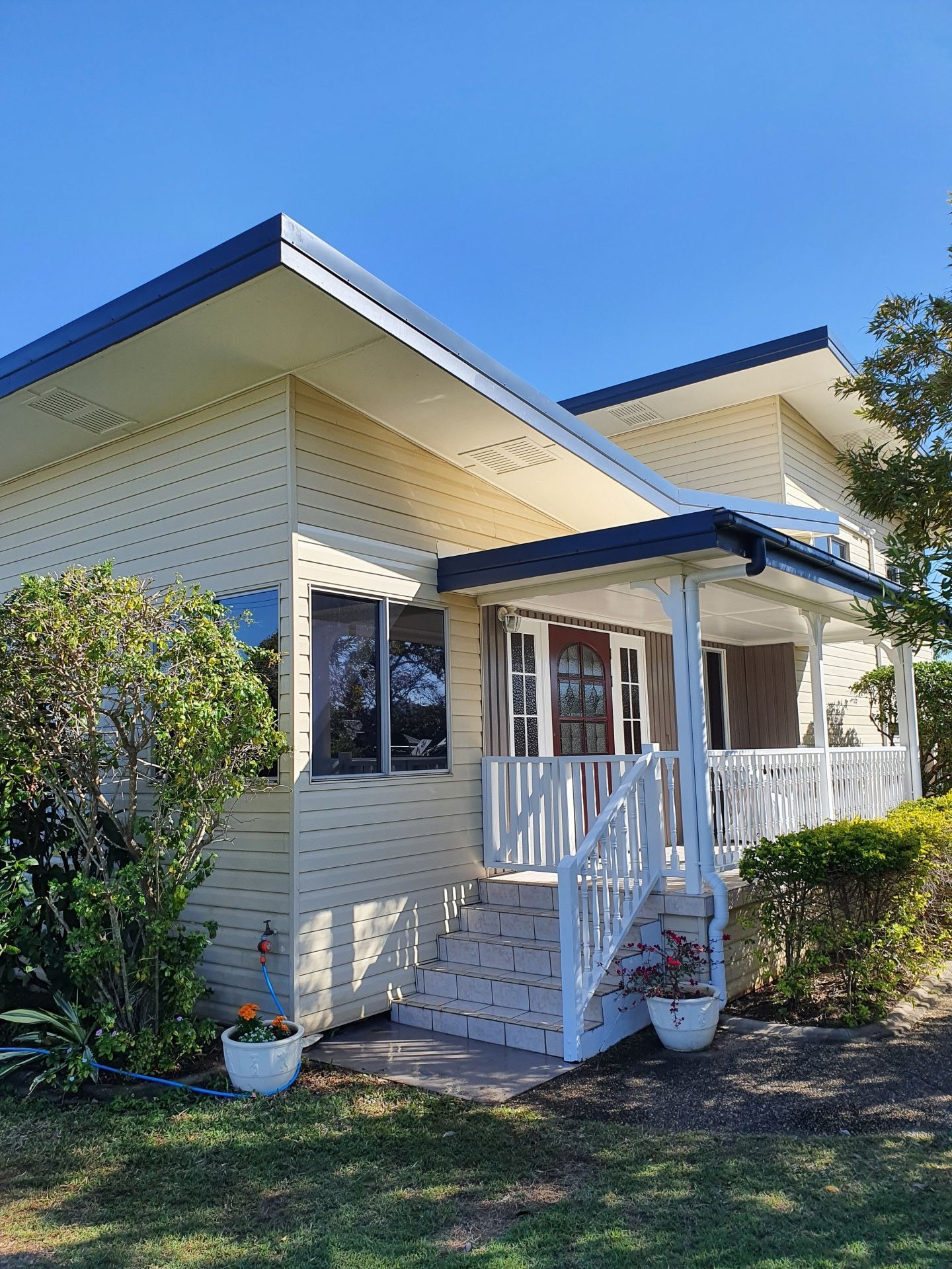 A light yellow house with a white porch and blue roof under a clear blue sky.— Keppel Coatings in Pacific Heights, QLD