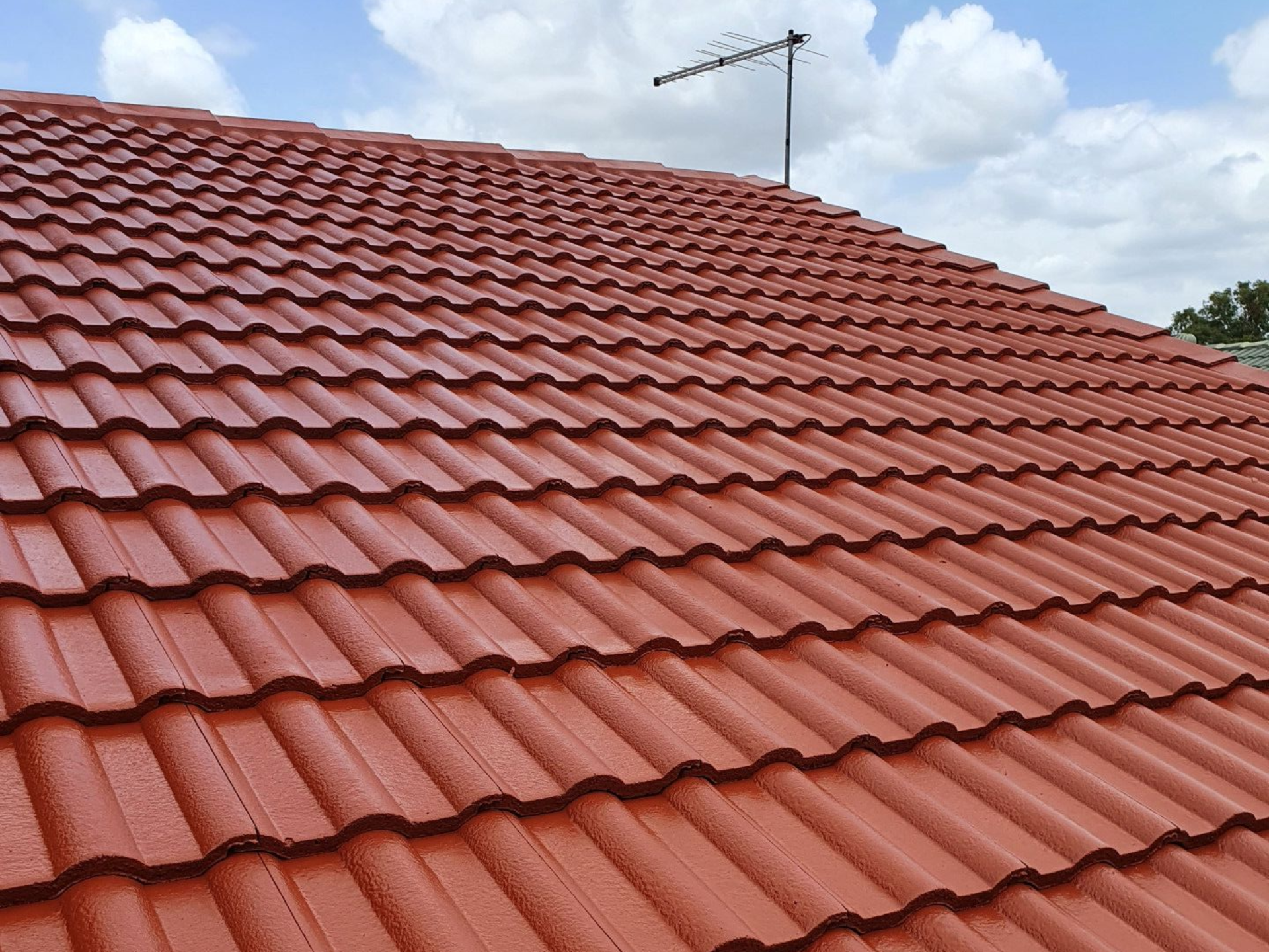 Red tiled roof with a rooftop antenna against a cloudy sky.— Keppel Coatings in Pacific Heights, QLD