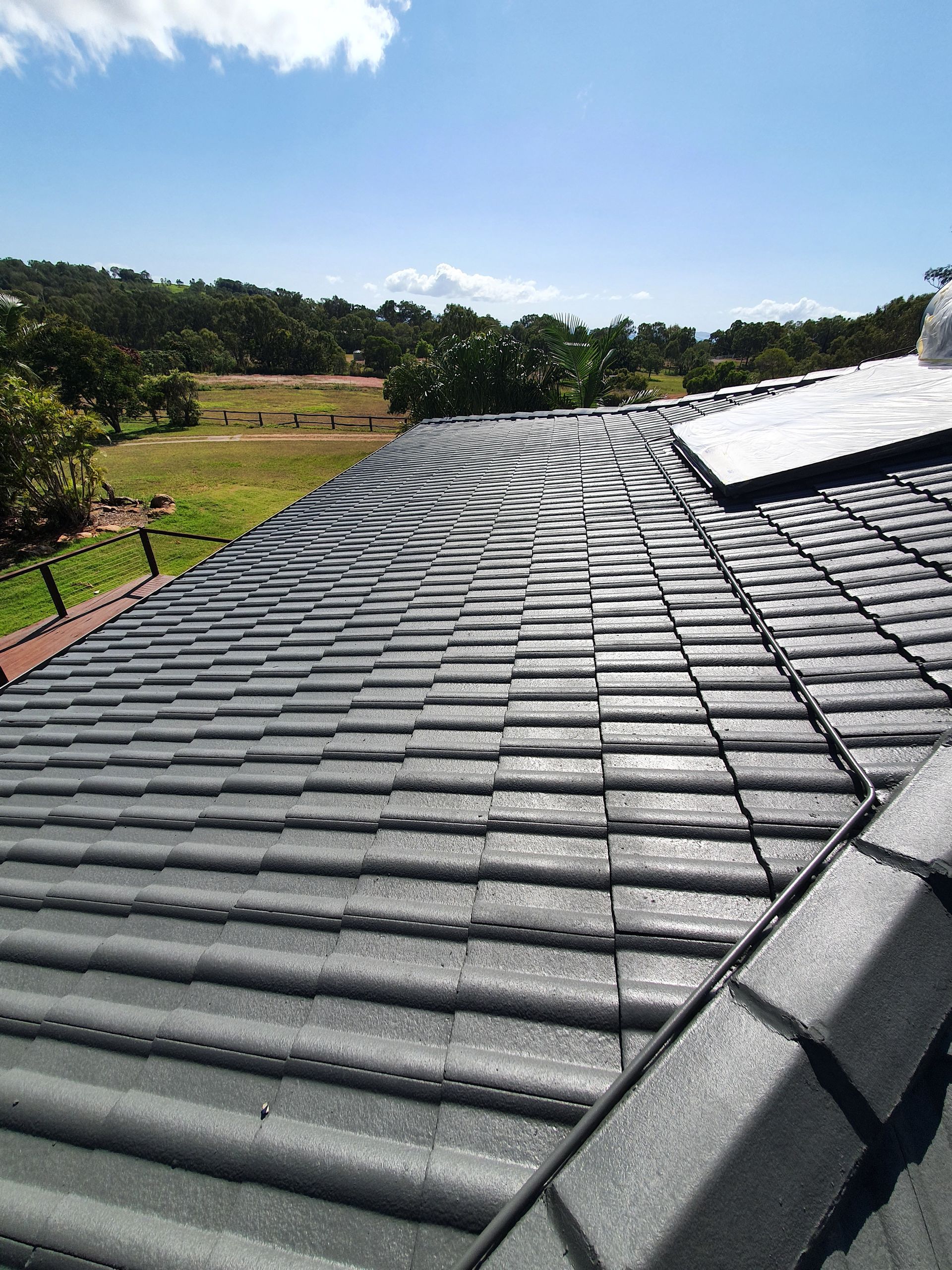 Gray Tile Roof With Curved Ridge Against a Sunny Sky — Keppel Coatings in Pacific Heights, QLD