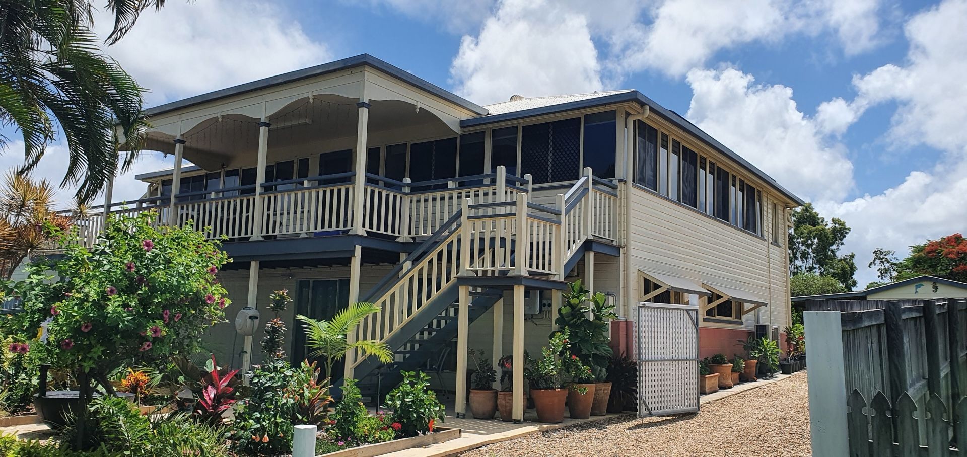 Two-story beige house with veranda, stairs, and plants, under a blue sky.— Keppel Coatings in Pacific Heights, QLD