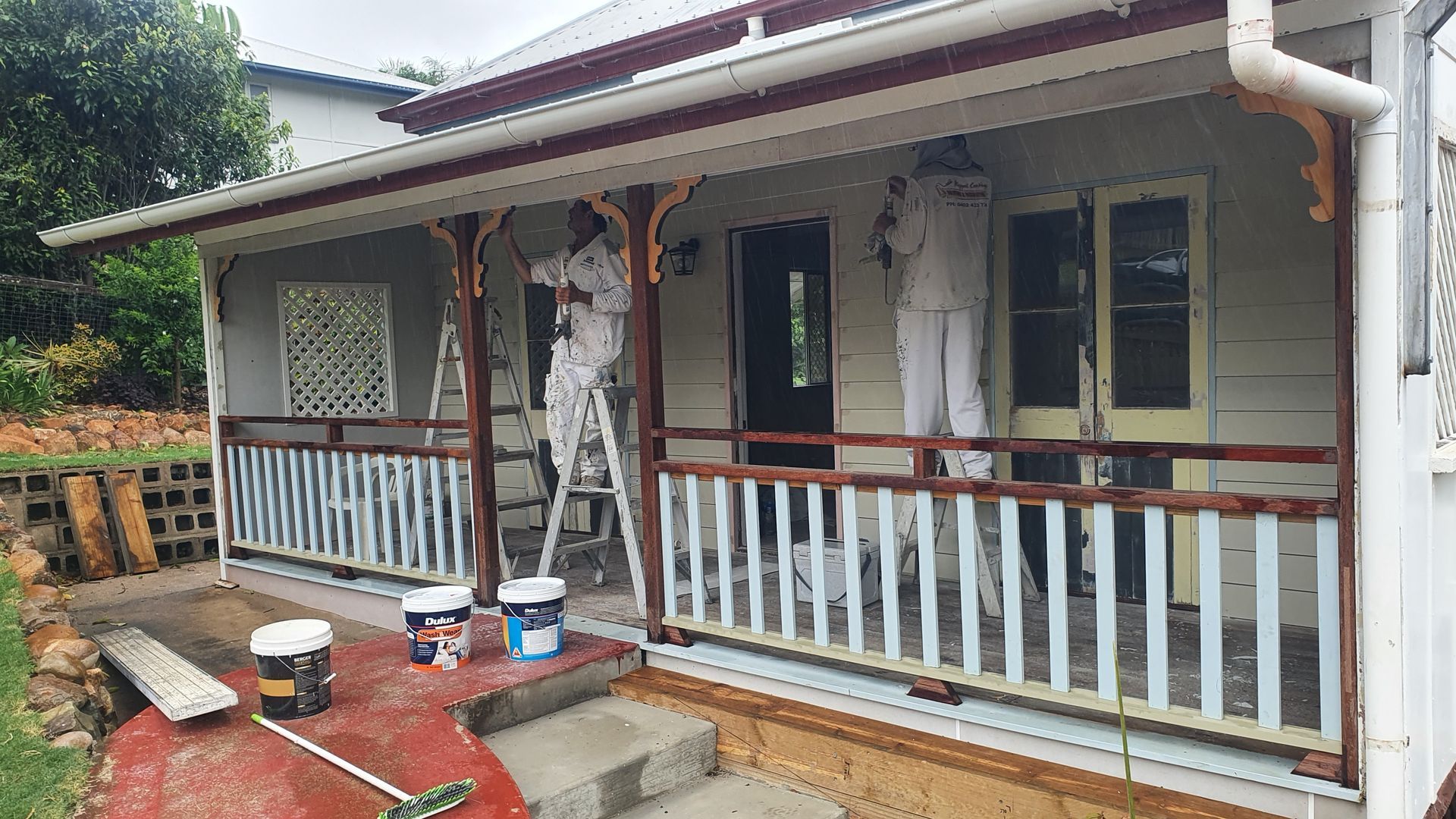 Two Painters on Ladders Painting a House Porch White and Brown — Keppel Coatings in Pacific Heights, QLD
