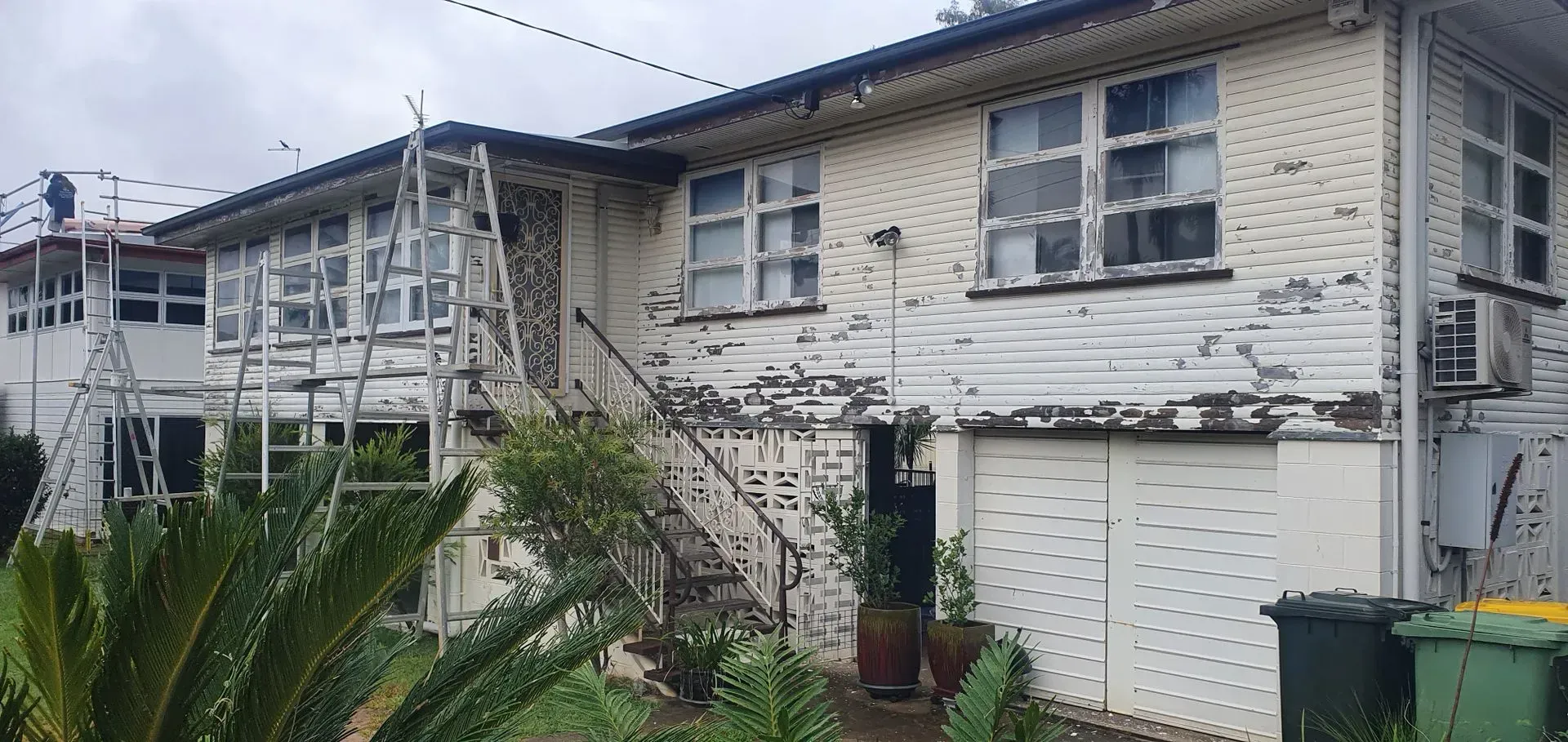 Two-story House With Peeling White Paint and Metal Scaffolding — Keppel Coatings in Pacific Heights, QLD