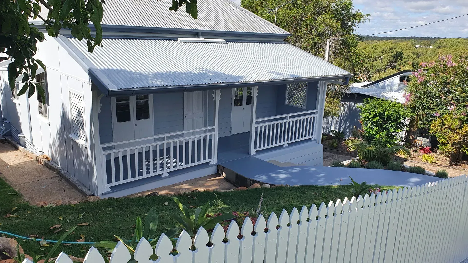 Blue and White Cottage With a Porch, White Picket Fence, and Greenery — Keppel Coatings in Pacific Heights, QLD