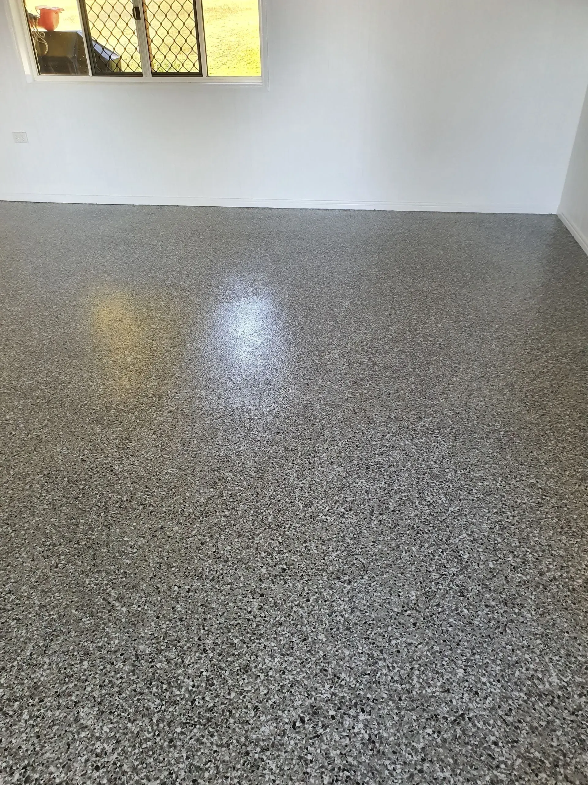 Gray Speckled Epoxy Flooring in a Room With White Walls and a Window — Keppel Coatings in Pacific Heights, QLD