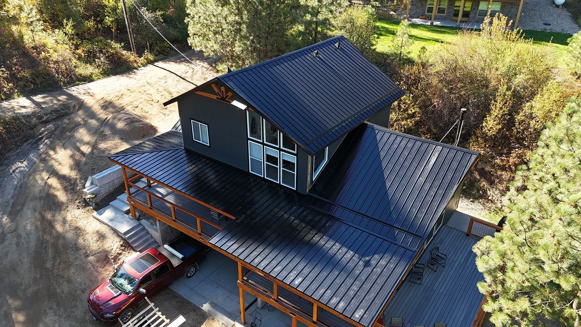 Modern black house with deck and red car in a natural setting.