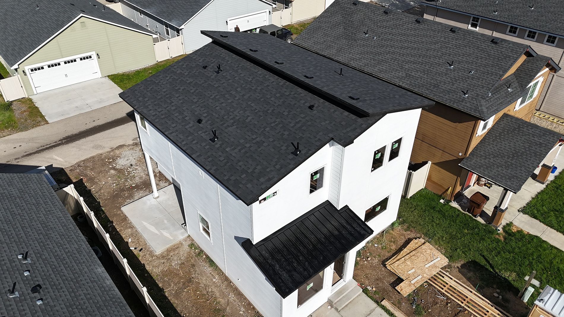 Two-story white house with black roof in a residential neighborhood.