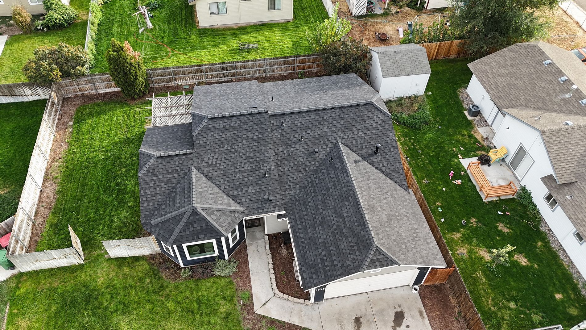 Overhead view of a house with a dark roof, surrounded by green grass and a concrete driveway.