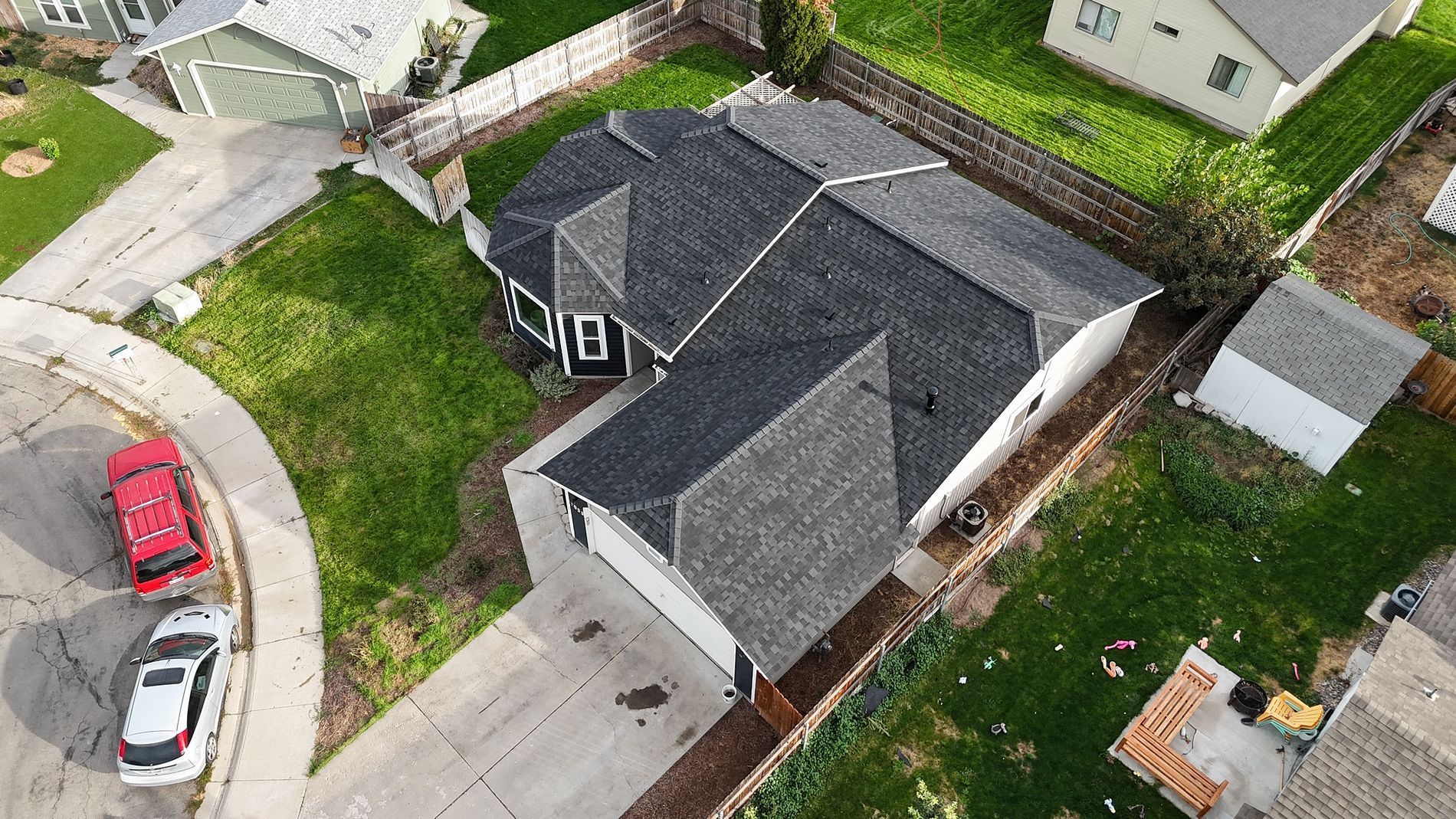 Overhead view of a gray-roofed house with a concrete driveway and grassy yard, cars parked on the street.