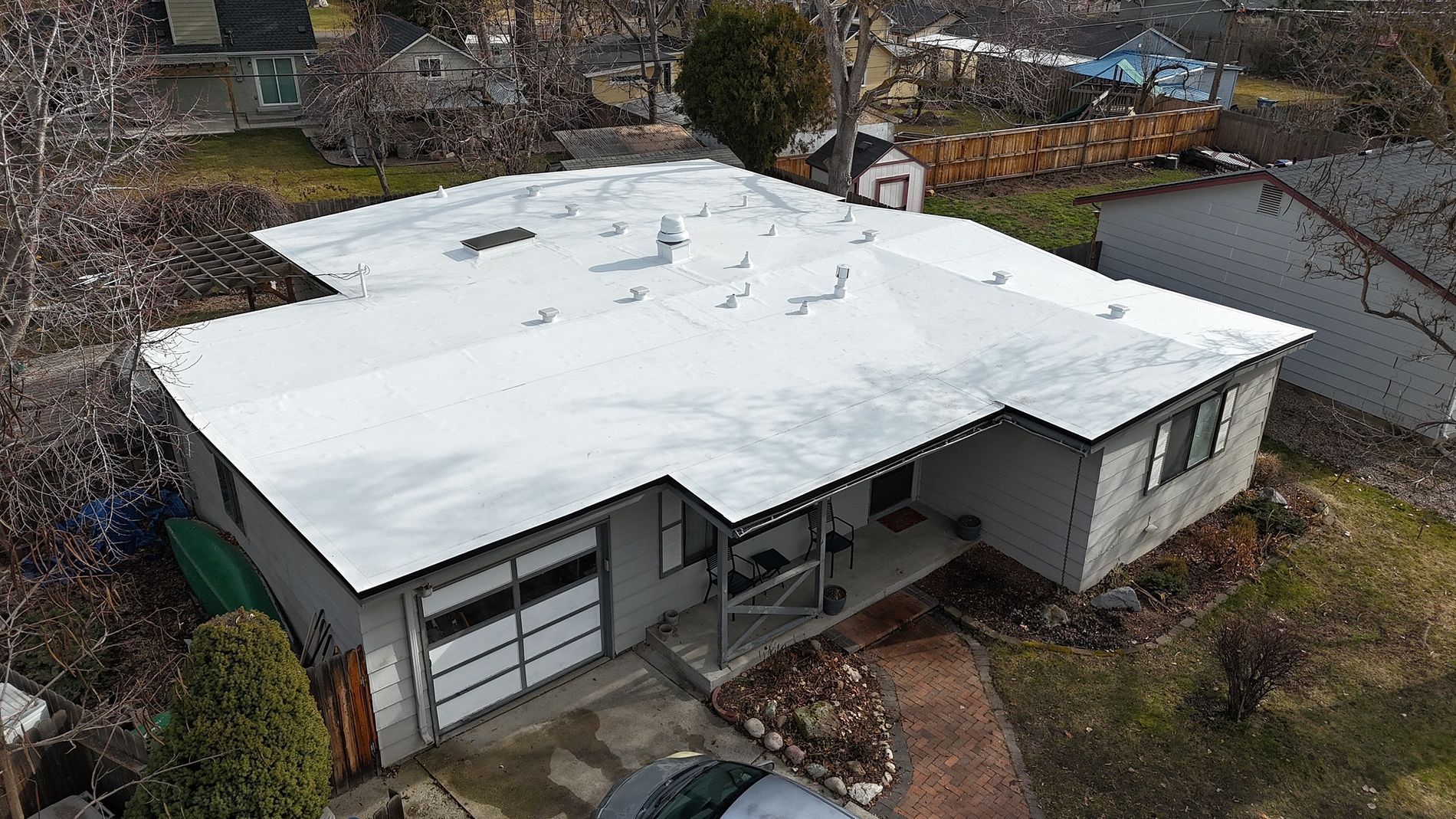 Flat rooftop with white and brown roofing materials, construction underway, distant trees, sunny.