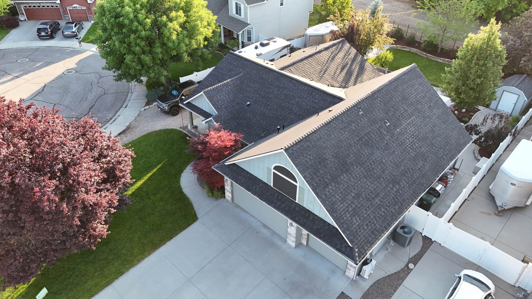 Aerial view of a two-story house with a gray roof and driveway, trees, and a car parked.
