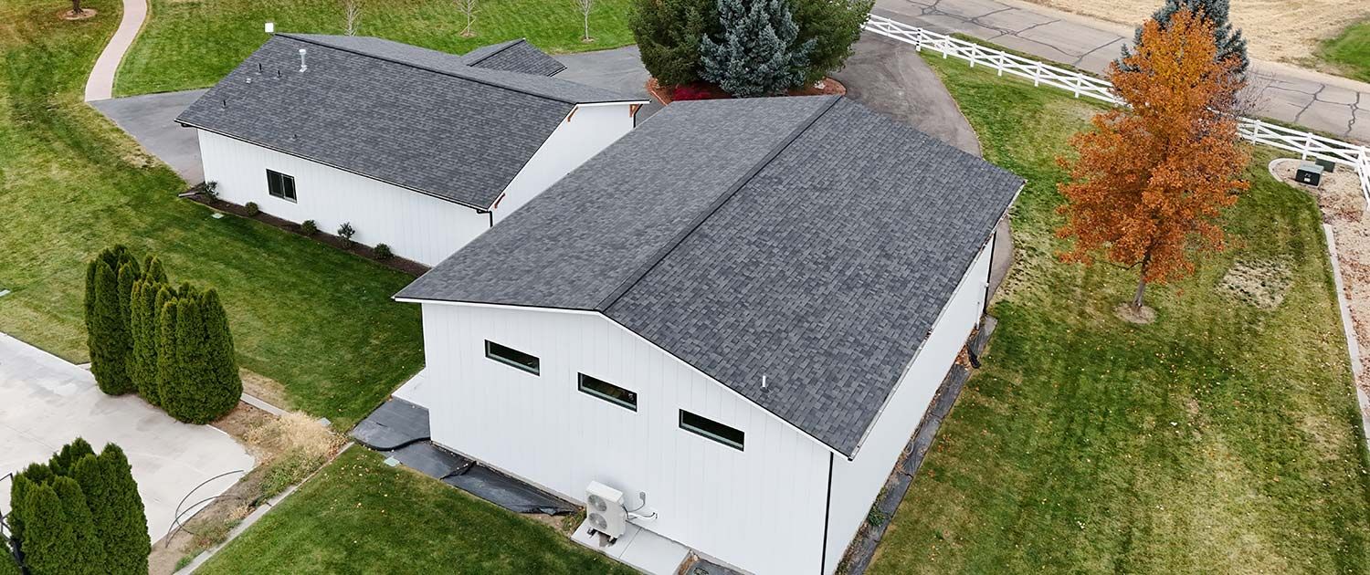 White buildings with dark gray roofs are surrounded by green grass and trees.