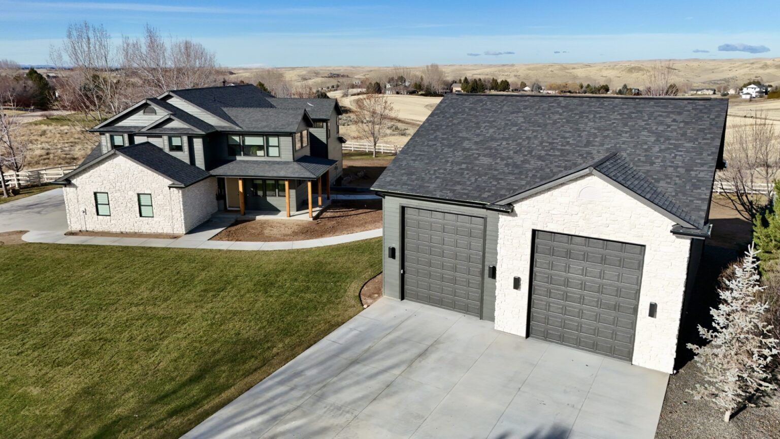 Modern two-story house and two-car garage with gray and white exterior on a grassy lot under a blue sky.