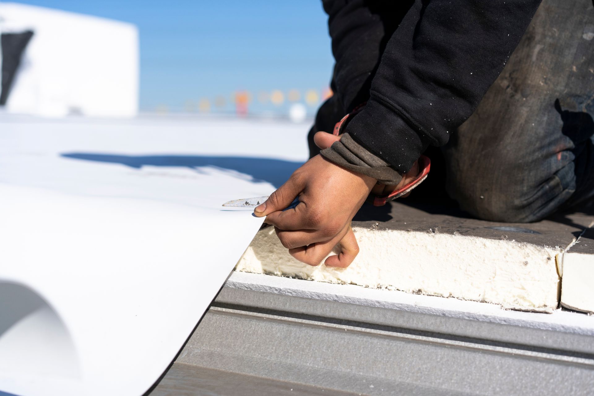 Person on a rooftop installing white roofing material, pulling back the edge to secure it.