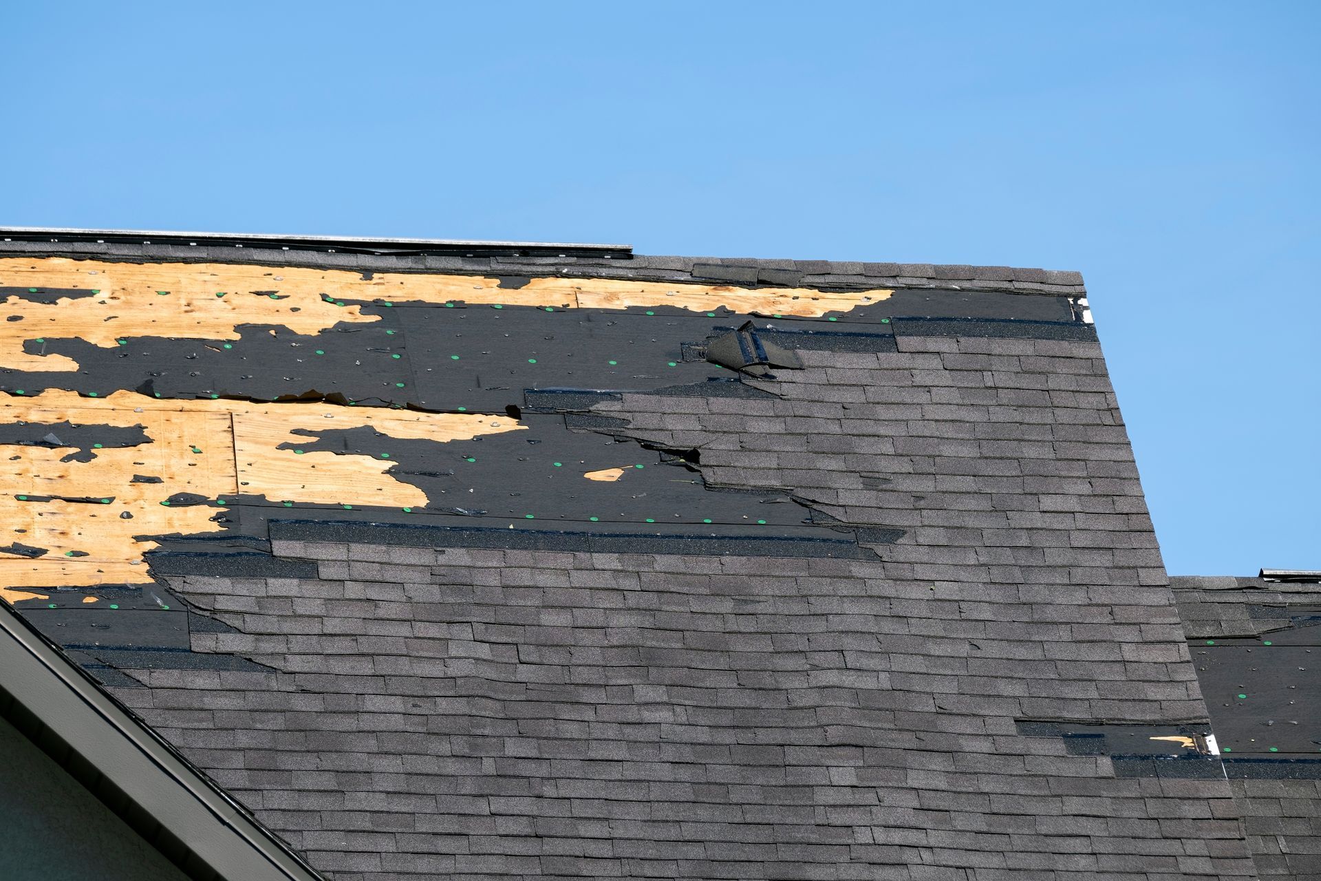 Damaged asphalt shingle roof, with missing shingles and exposed underlayment.