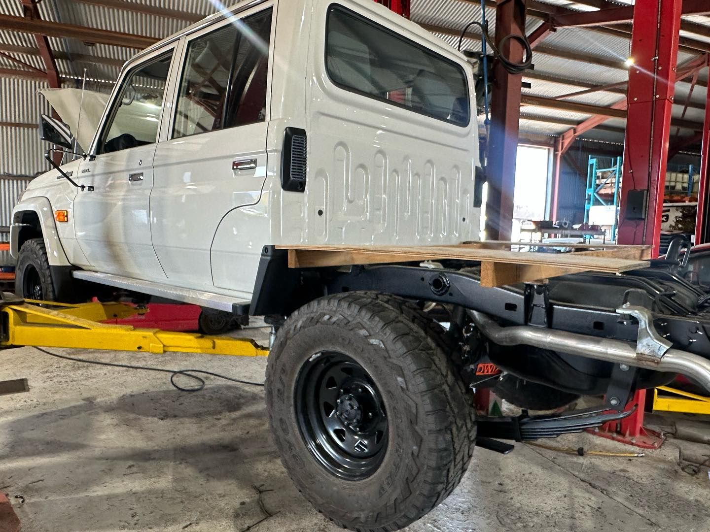 White truck cab on a chassis in a garage, with a wooden bed. Black wheels, red accents — E.C.A Mechanical Repairs in Paget, QLD