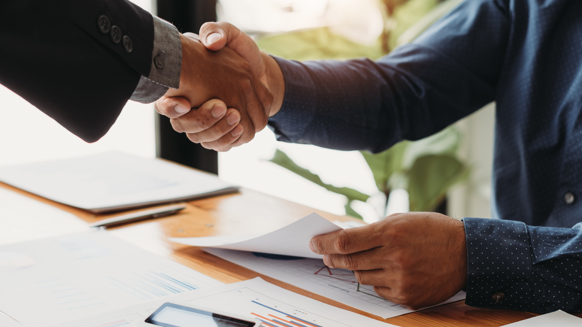 Two men are shaking hands over a table.