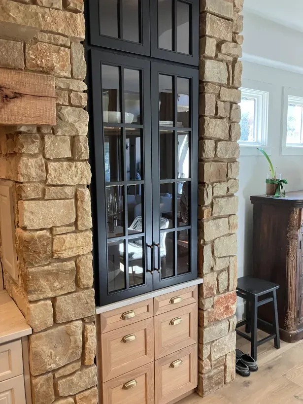 A kitchen with a stone wall and black cabinets.