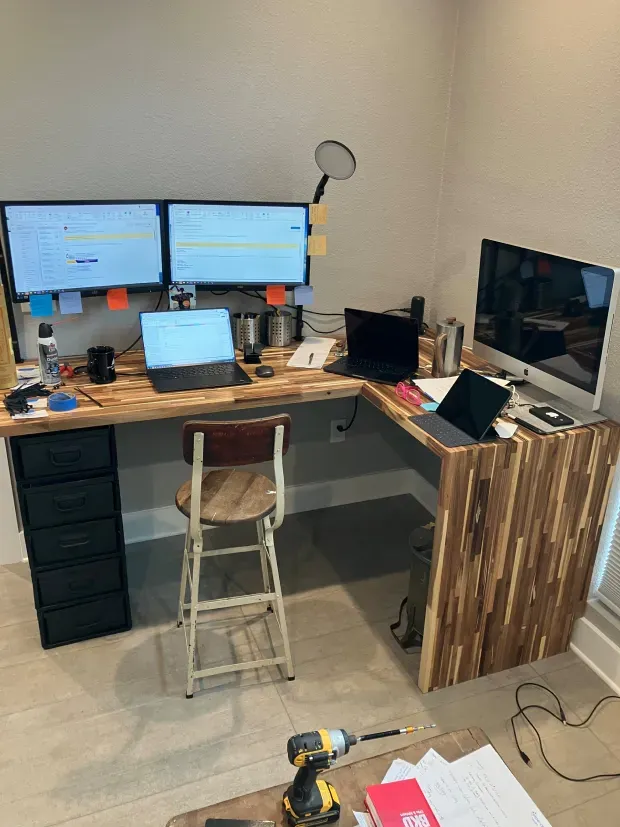 A wooden desk with two computer monitors and a laptop on it.