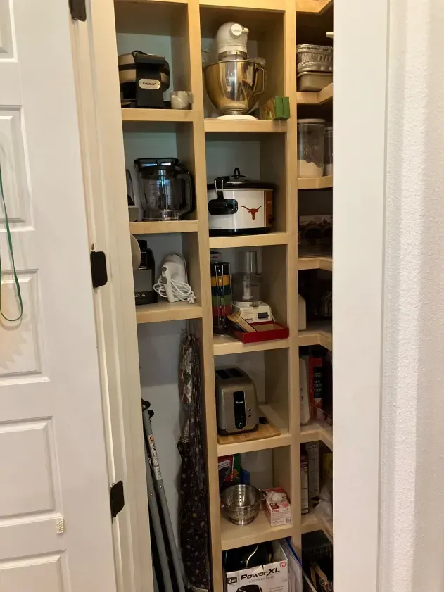 A pantry filled with lots of kitchen appliances and a vacuum cleaner.