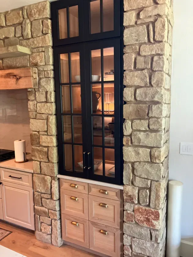 A kitchen with a stone wall and wooden cabinets