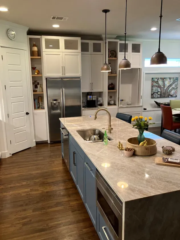 A kitchen with a large island , sink , refrigerator and dishwasher.