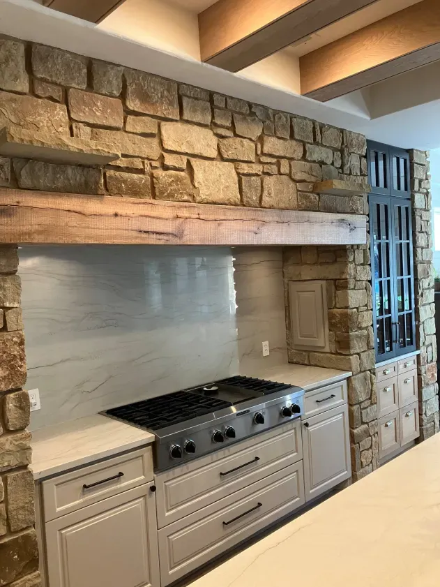 A kitchen with a stove top oven and a stone wall.