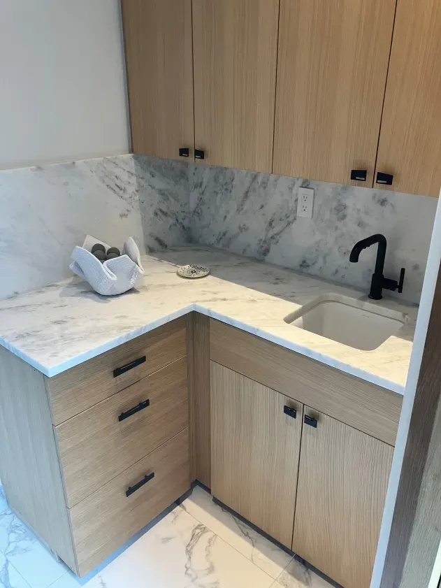 A kitchen with wooden cabinets , marble counter tops and a sink.
