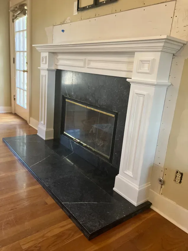 A fireplace with a black tile surround and a white mantle in a living room.