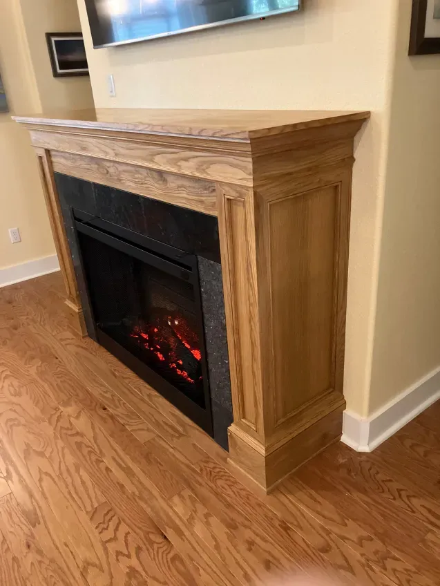 A fireplace with a wooden mantle is in a living room with hardwood floors.