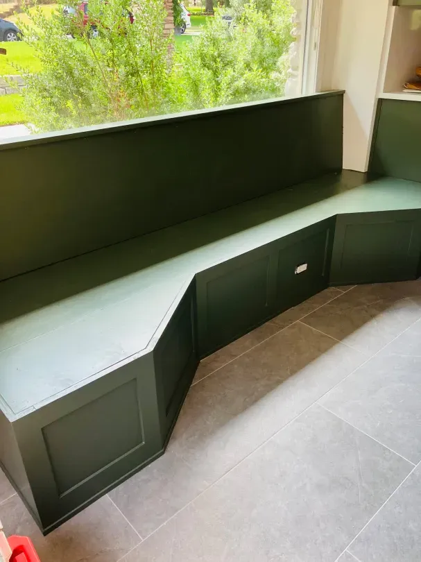 A green bench with drawers underneath it is in a room next to a window.