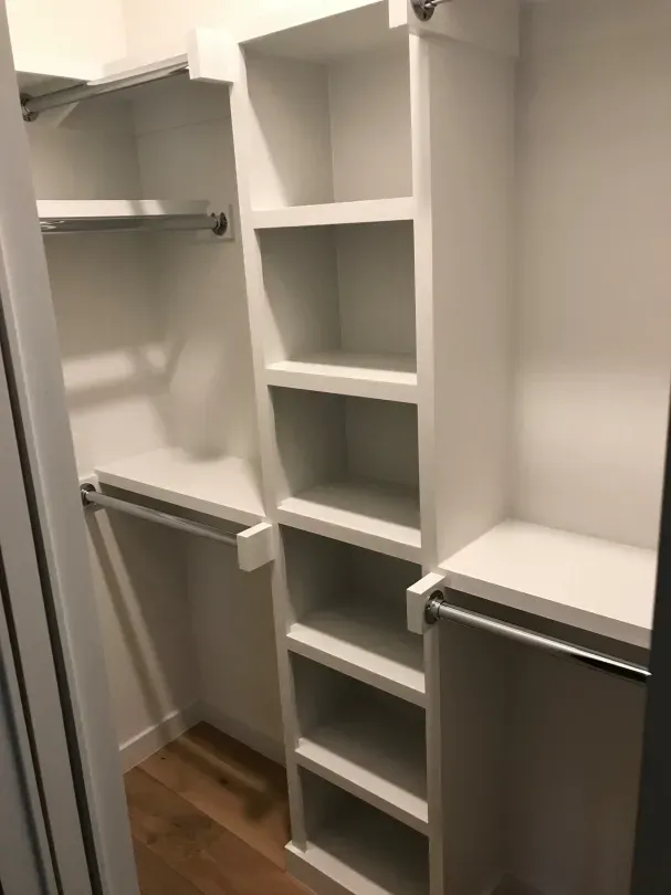 A walk in closet with white shelves and a wooden floor.
