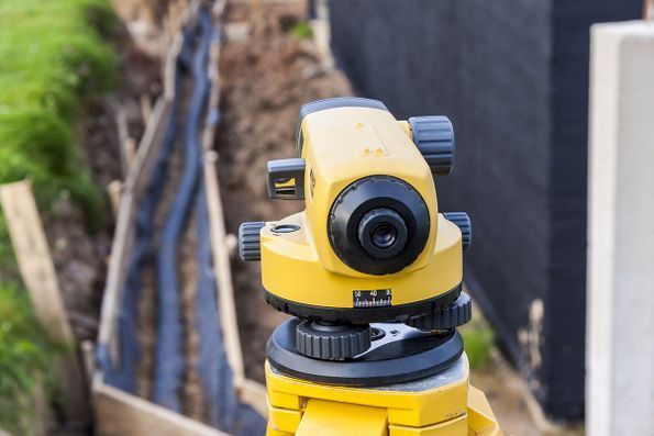 A yellow level is sitting on top of a tripod on a construction site.