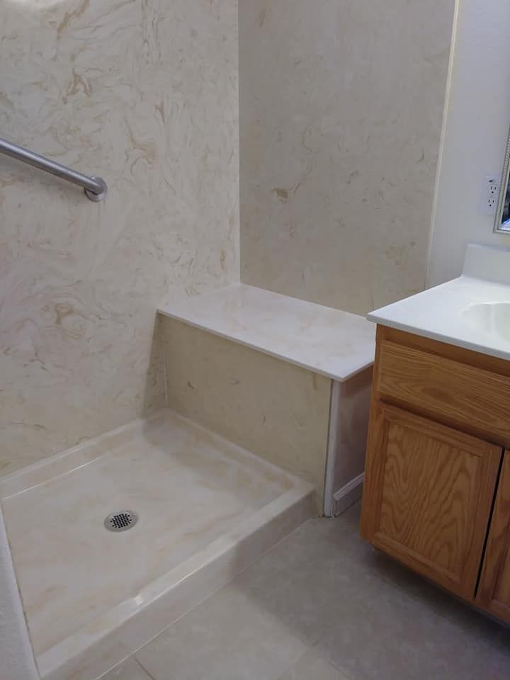 Accessible shower with built-in bench and handrail. Light beige walls and floor, wooden vanity.