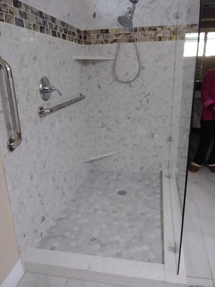 Accessible shower with white marble walls and floor, a grab bar, and glass door.
