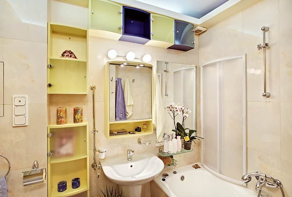 A small bathroom with yellow storage, a sink, a bathtub, and a shower.