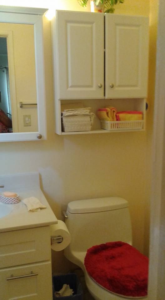Small bathroom with white cabinets, toilet, and red toilet seat cover.