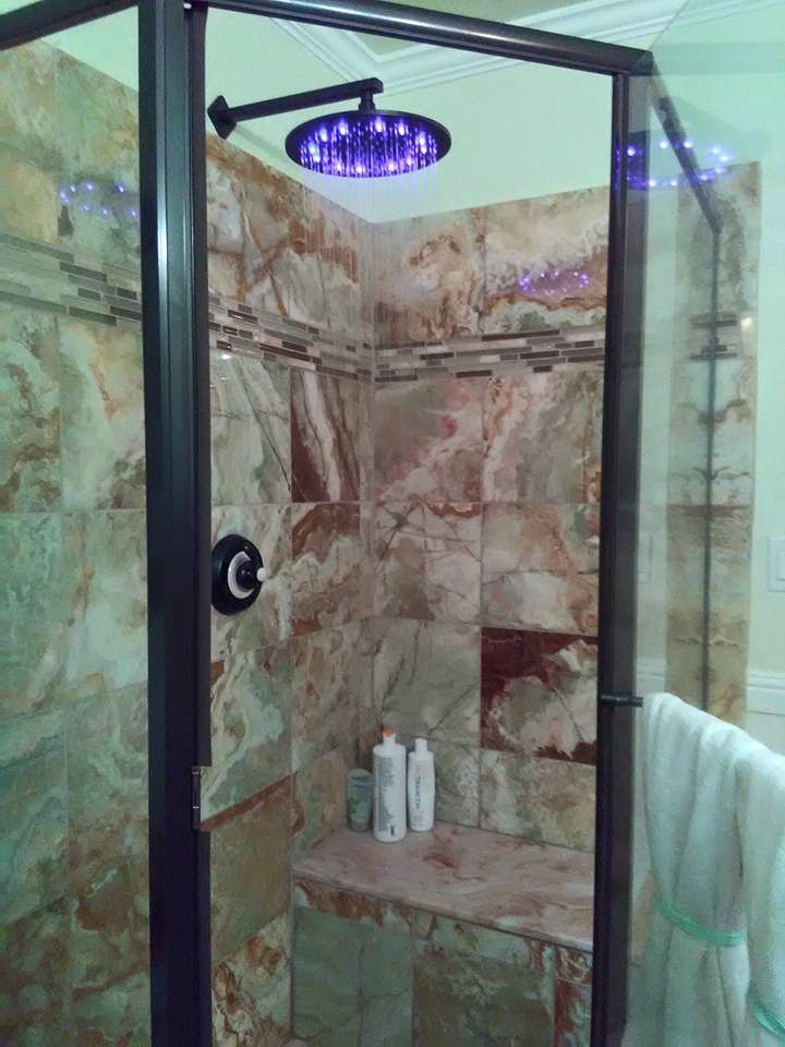 Shower with brown stone tile, glass door, dark metal frame, overhead showerhead, and a built-in seat.