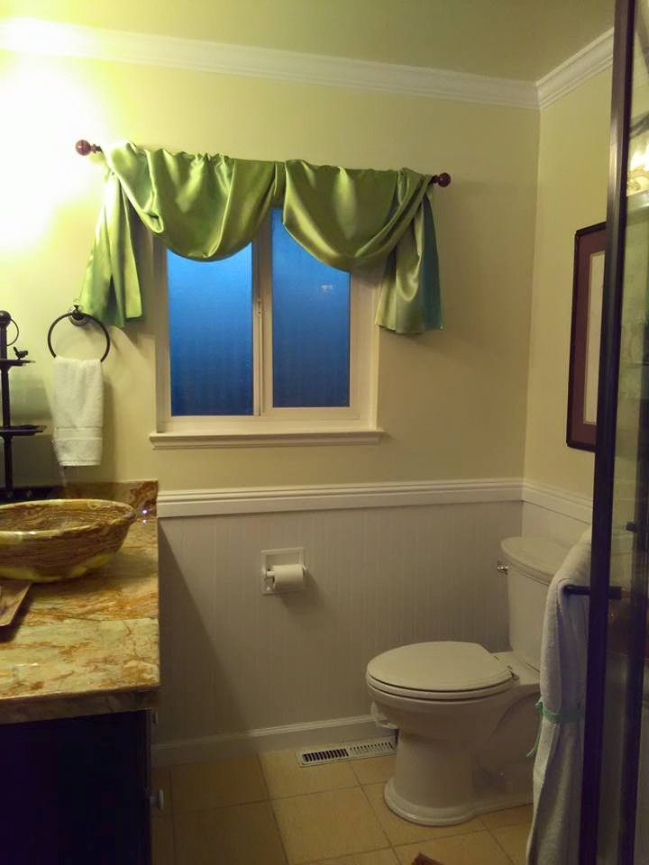 A bathroom with a toilet, sink, window, and green curtains. Beige walls and a tile floor.