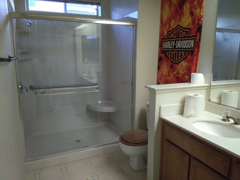 Bathroom with shower, toilet, vanity, Harley Davidson banner. Beige walls, brown vanity, and white fixtures.