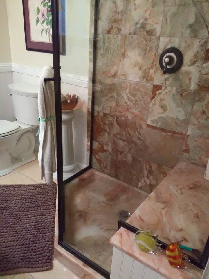Bathroom with shower, toilet, and rug. Brown tiled shower interior, glass door. Beige walls, light fixture.