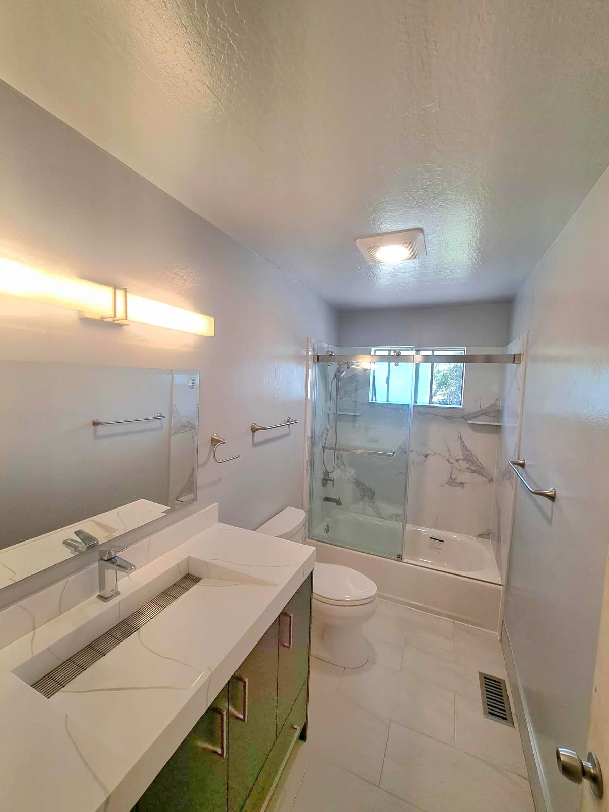 Modern bathroom with white and marble finishes, bathtub, vanity, and toilet.