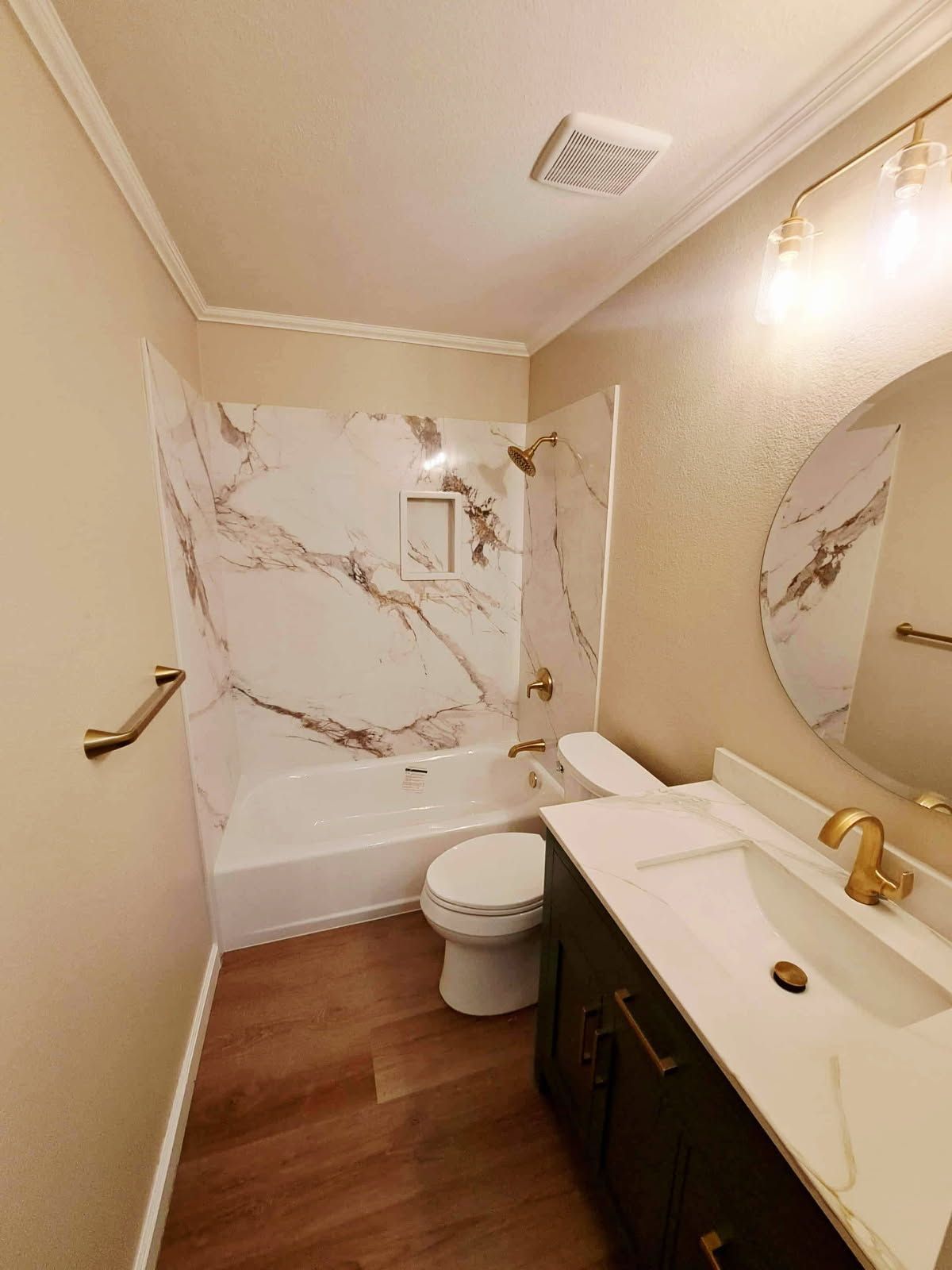 Bathroom with white marble shower, gold fixtures, dark vanity, and wooden floor.