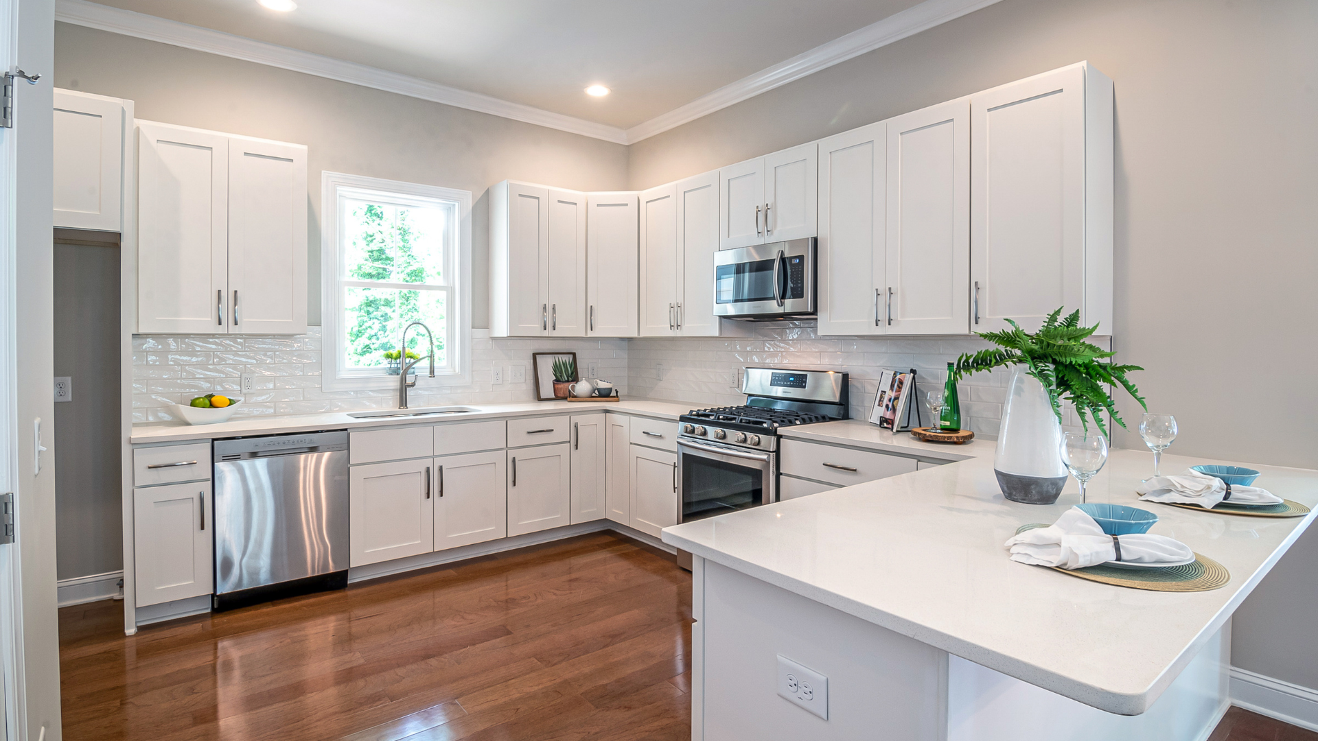 White kitchen with hardwood floors, stainless steel appliances, and a breakfast bar.